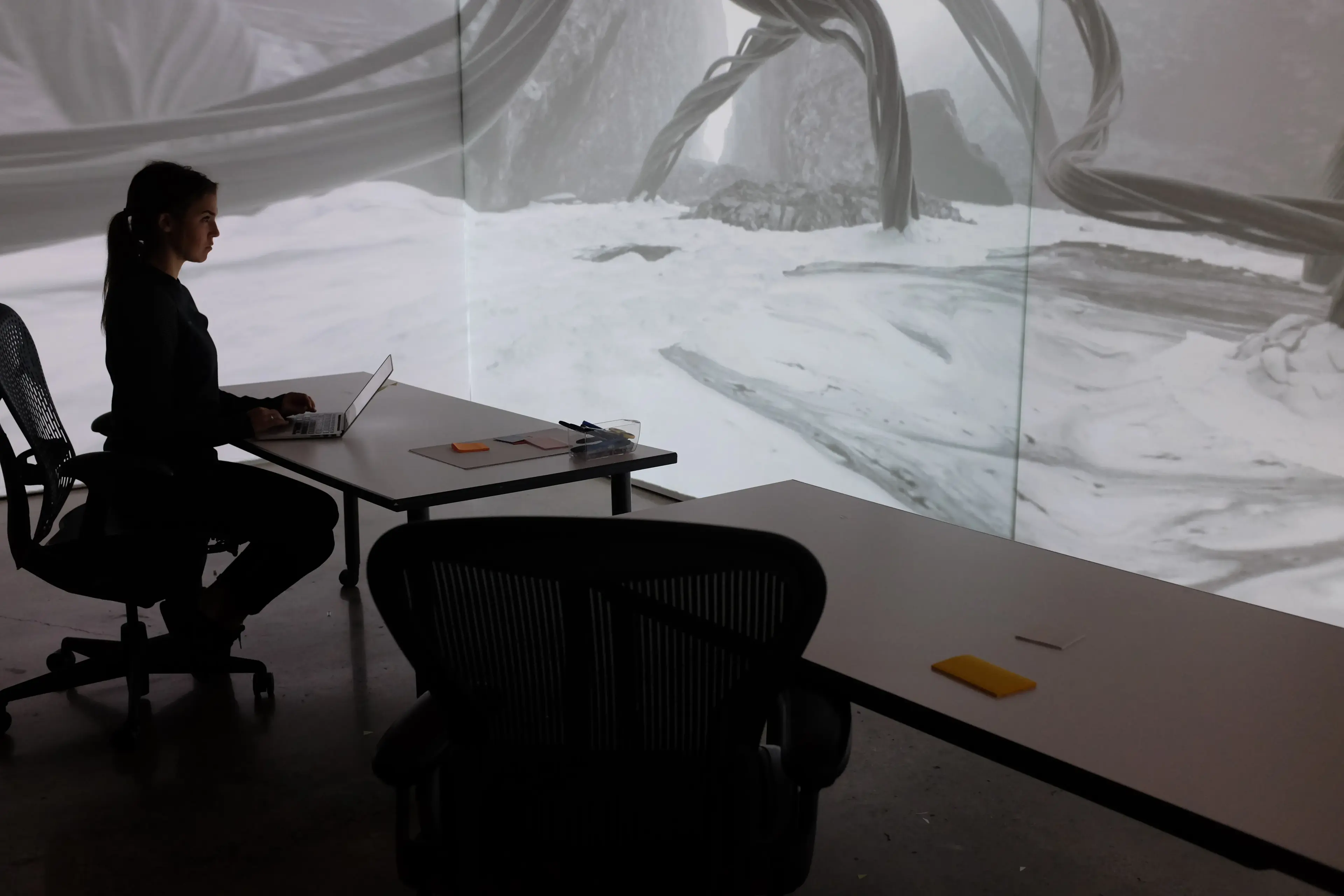 Alternate angle of the projection room showing the immersive 3D environment wrapping the corner walls, with a person working at a desk inside the space
