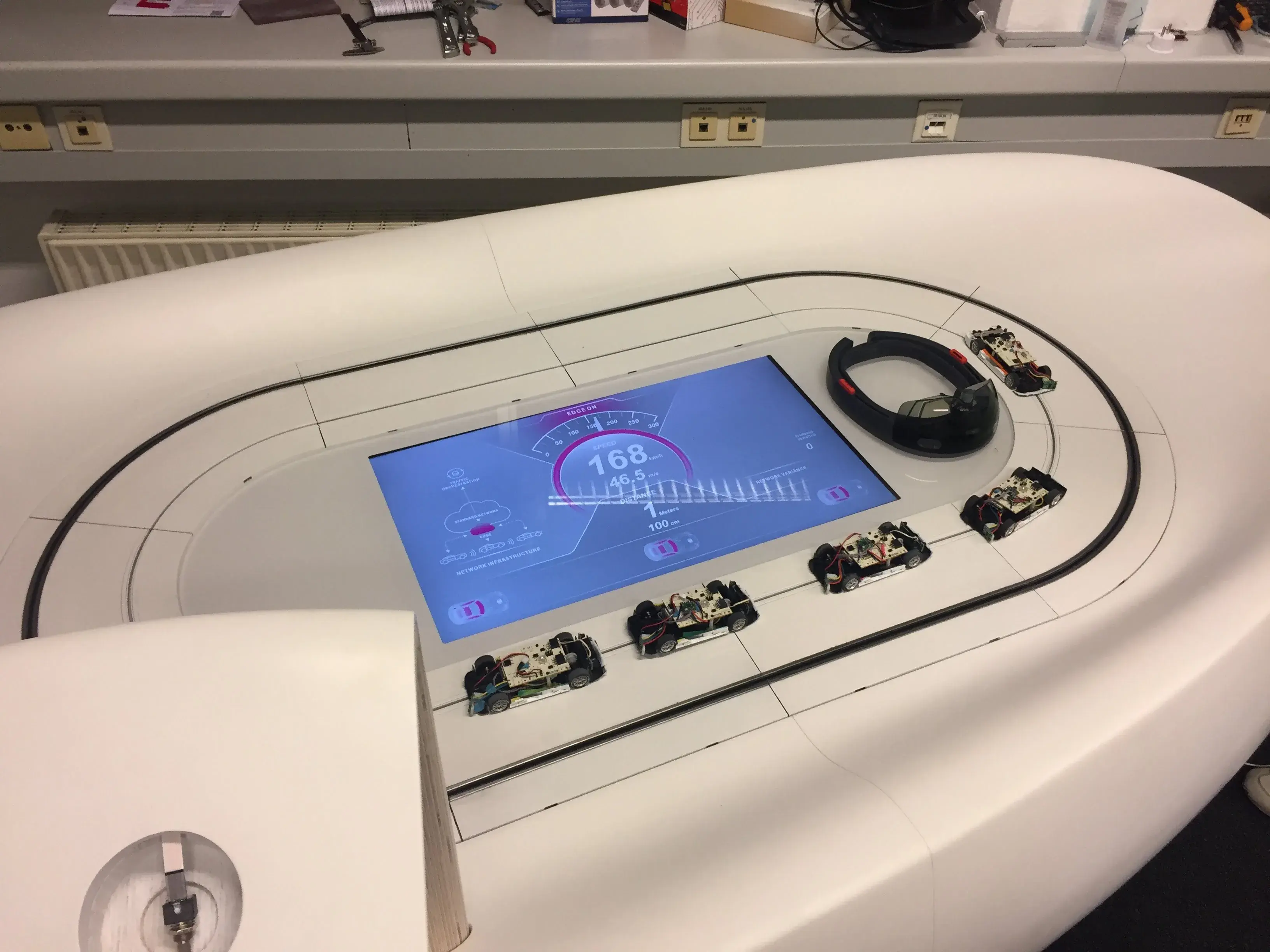 Final installation with sculpted white track, embedded display showing telemetry, and autonomous vehicles circling